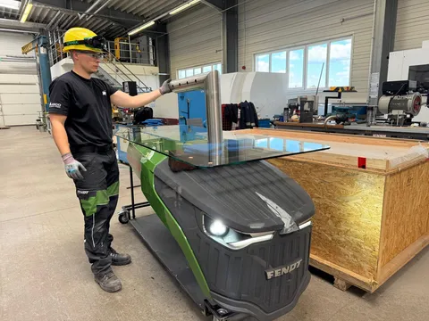 One man (apprentice) is standing at the Fendt dispensing station, which is next to a box, and is examining the tap on the dispensing station.