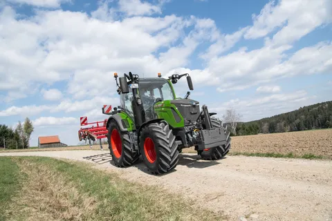A Fendt 300 Vario with cultivator in transport A green Fendt 300 Vario driving with a red cultivator on a field path.