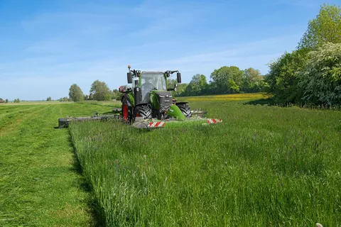 Fendt 300 Vario mowing with Fendt Slicer mower combination in grassland. A green Fendt 300 Vario mowing with Fendt Slicer front & rear mowers in grassland.