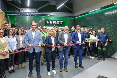 A group of people, including four individuals in the foreground holding large scissors, cut a red ribbon in front of a Fendt sign in the new apprentice workshop.