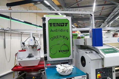 A green sign with the inscription "Fendt apprenticeship" hanging above machines in the Fendt training workshop.