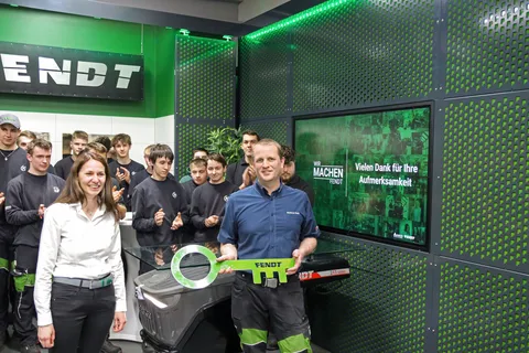 A woman on the left and a man on the right in the foreground, the man is holding a large green key with the inscription Fendt.