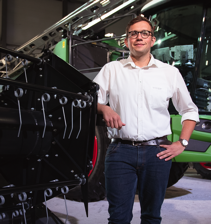 Florian Langenbuch stands next to a Fendt tractor and looks into the camera
