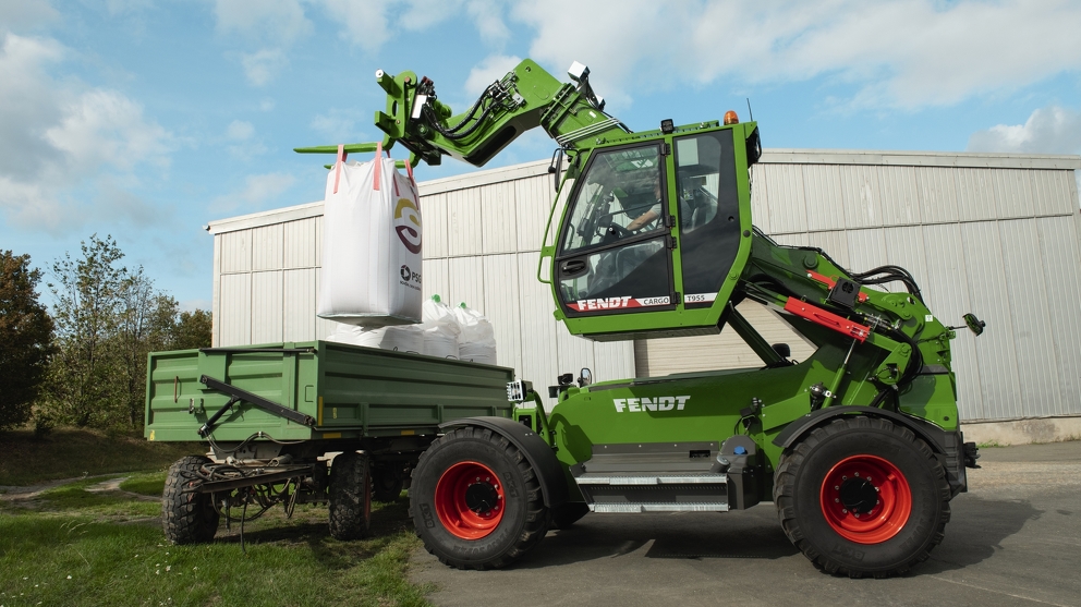 The extended Fendt Cargo T955 loads a loading vehicle in front of a storehouse.