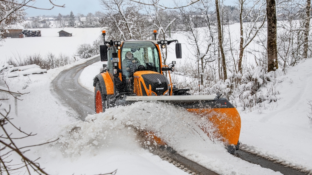 Orange Fendt tractor removes snow on a road in a snowy landscape Orange Fendt tractor removes snow on a road in a snowy landscape