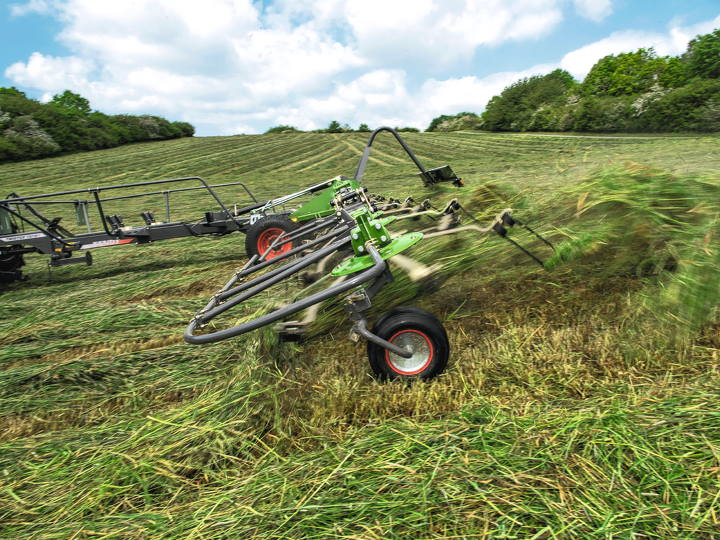Fendt Twister tedder on a field during turning. Grass flies into the air.