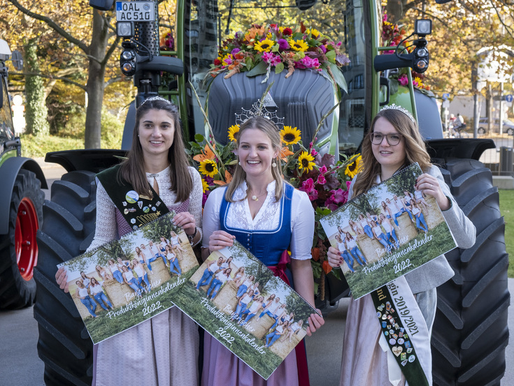 Three highnesses with calendars in front of a Fendt tractor with flower decoration
