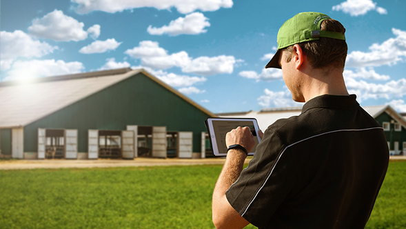 A farmer with a tabler stands in front of his farm and subscribes to the newsletter
