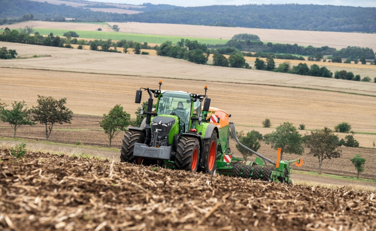 A Fendt 728 Vario with an implement on a field further fields and forests in the background