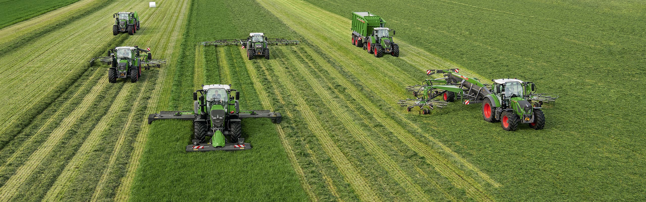 Several Fendt tractors with different implements drive side by side in a field