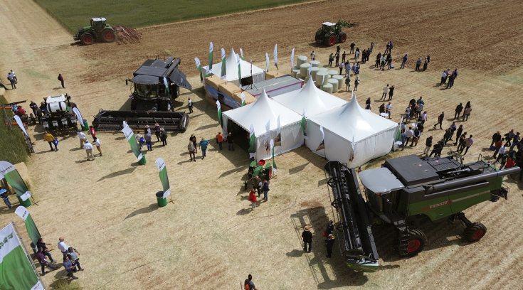 Tents with Fendt combines and tractors all around on a field