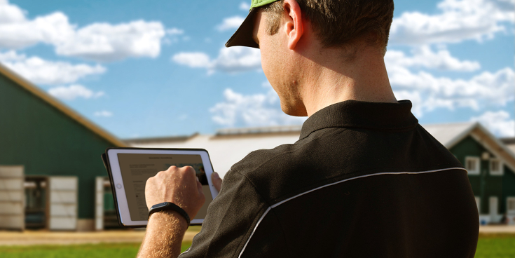 A farmer stands in front of his farm with tablet in hand and is signing up for the Fendt newsletter