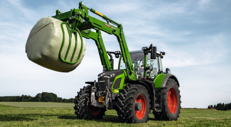 Fendt 600 Vario tractor with frontloader carrying a silage bale on a pasture