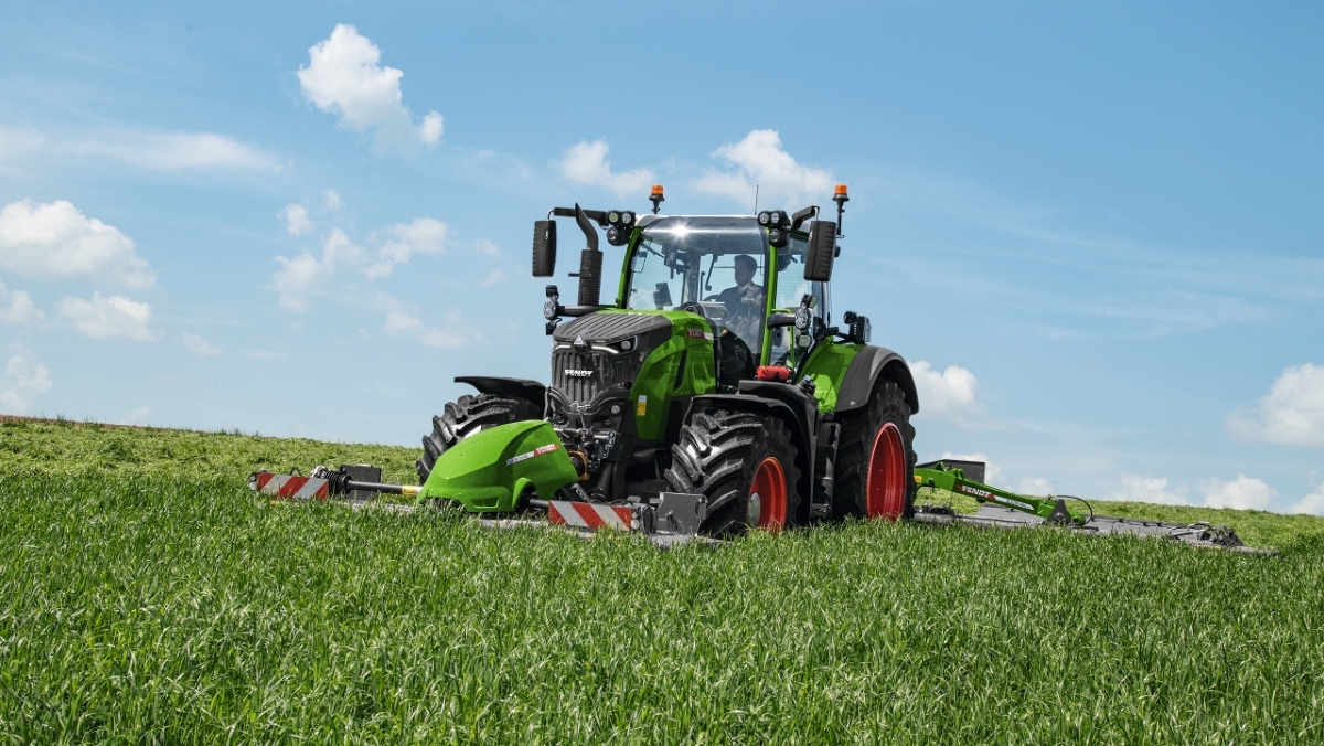 A farmer driving a Fendt 700 Vario Gen7 in the meadow and mowing with a Fendt Slicer mower