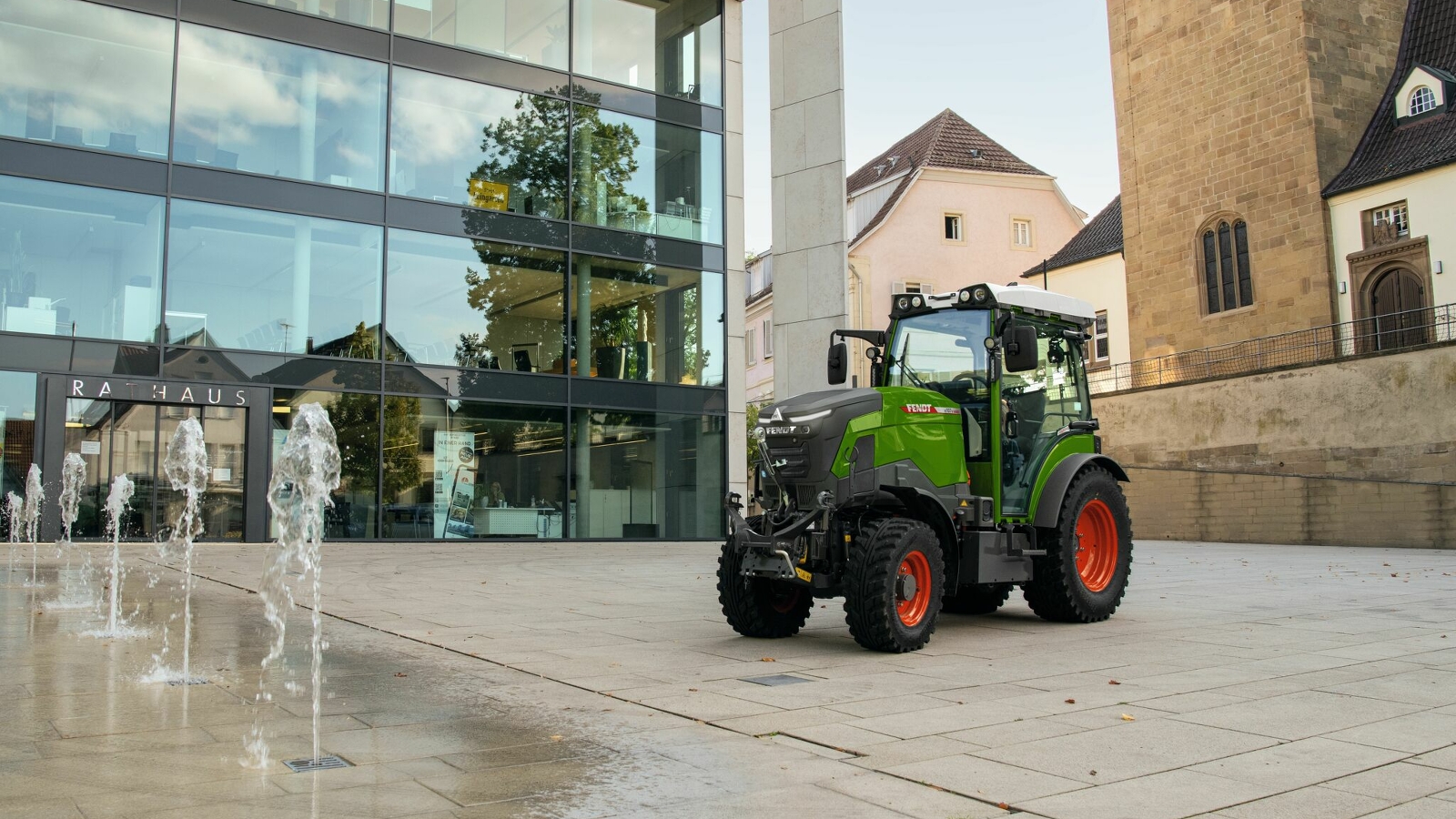Fendt e100 V Vario for municipal use in the city A green Fendt e100 V Vario with red rims standing in front of a building in the city