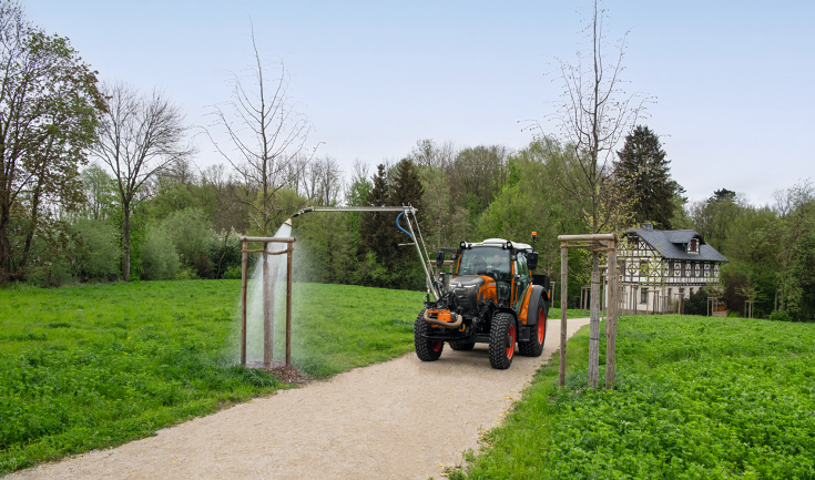 Fendt e100 Vario watering trees A Fendt e107 Vario in municipal orange waters a tree in a park in spring with a watering arm attached to the front of the tractor. An old, renovated half-timbered house can be seen in the background.