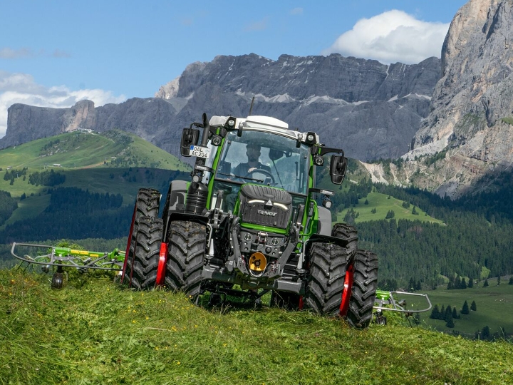 Fendt 200 Vario The Fendt 200 Vario with double tyres and red rims driving on a green mountain meadow, with mountains and blue sky in the background