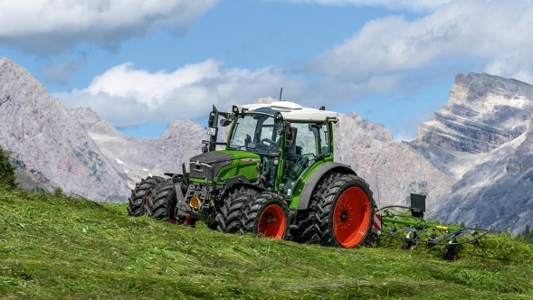 Fendt 200 Vario The green Fendt 200 Vario tractor with red rims and dual tyres is at work on a mountain meadow with a blue sky, white clouds and mountains in the background.