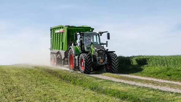 Fendt 600 Vario Der grüne Fendt 600 Vario Traktor mit roten Felgen und dem grünen Ladewagen Fendt Tigo fährt auf einer kleinen Feldstraße mit einer grünen Wiese im Vorder- und Hintergrund.