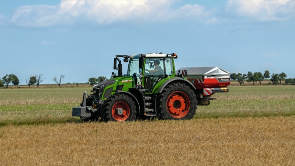 Fendt 600 Vario Der grüne Traktor Fendt 600 Vario mit roten Felgen in seitlicher Ansicht auf einer grünen Wiese. Ein blauer Himmerl mit weißen Wolken ist im Hintergrund zu sehen.