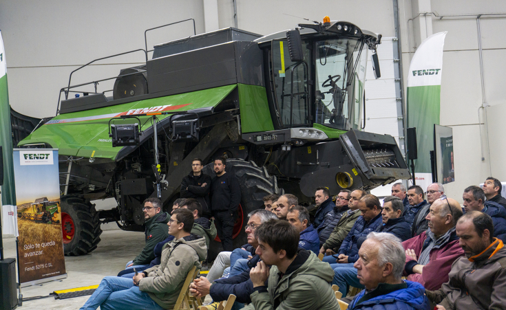 Fendt 6335 C PLI straw walker combine harvester Farmers are sitting on chairs in a hall looking at a stage; in the background (to the right of the farmers) is a Fendt straw walker combine in green; the photographer is standing to the left of the seated farmers