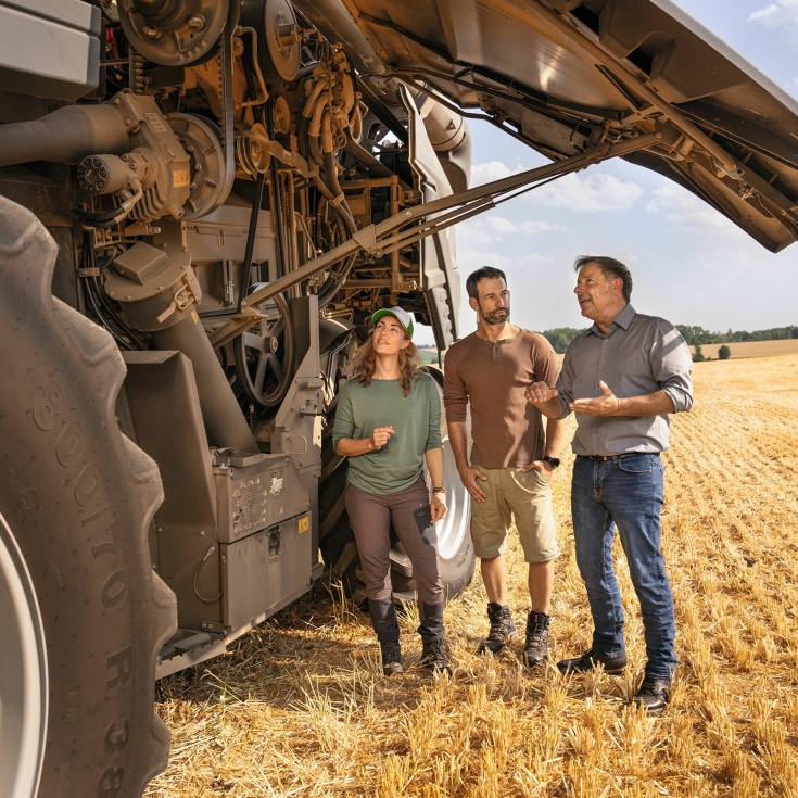 A Fendt dealer explains to a couple of farmers in a field how the Fendt combine harvester works.