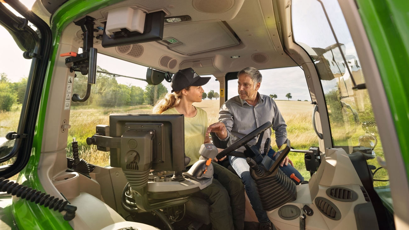 A Fendt dealer in the cab of a green Fendt 700 Vario Gen7 tractor demonstration model at the farmer customer's property