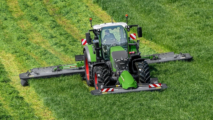 The green Fendt 600 Vario tractor mowing with the green Fendt Slicer implement on a green meadow; the mowing tracks can be seen in the background.
