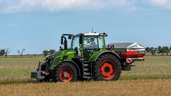 The green Fendt 600 Vario tractor with red rims seen from the side on a green meadow. A blue sky with white clouds can be seen in the background.