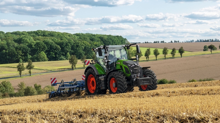 A green Fendt tractor with red rims tilling the soil in a harvested field with rolling hills in the background