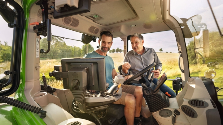 A Fendt dealer in the cab of a green Fendt tractor demonstration model at a farmer customer's property