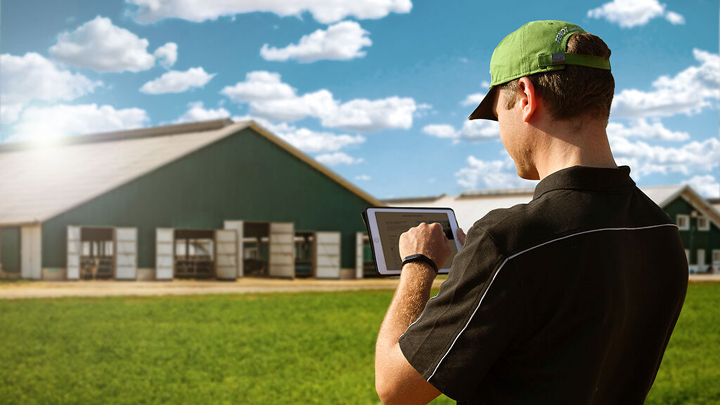 A farmer stands in front of his farm with tablet in hand and is signing up for the Fendt newsletter