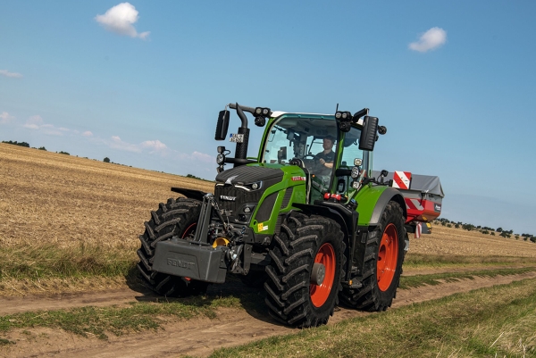The green Fendt 600 Vario tractor with red rims driving along a small country road with a light blue sky in the background.