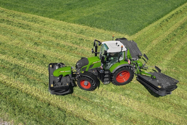 A bird's eye view of the green Fendt 600 Vario tractor with red rims and the Fendt Slicer mower in operation on a large green meadow.
