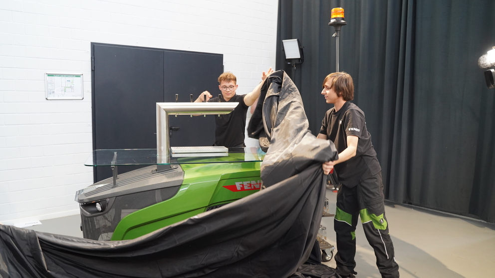 Two apprentices pull on a black cloth, revealing the Fendt dispensing station