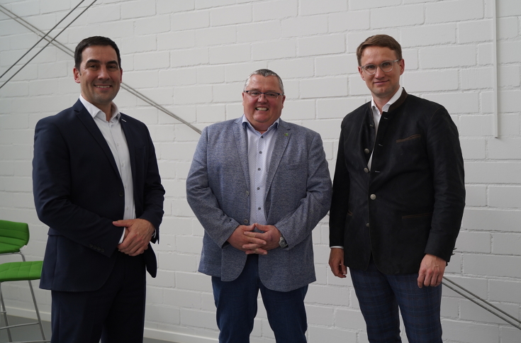 Three men smile for the camera in front of a white wall