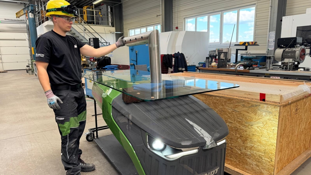 One man (apprentice) is standing at the Fendt dispensing station, which is next to a box, and is examining the tap on the dispensing station.