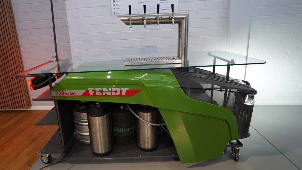 Fendt drinks dispenser (side view) with Fendt logo, castors, 4 taps, a glass shelf and front and rear lights switched on.