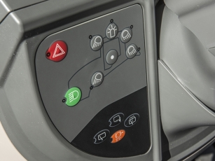 Detailed view of the left side of the dashboard in the Fendt 900 Vario MT with symbol buttons for driving and work lights as well as a red hazard warning light switch