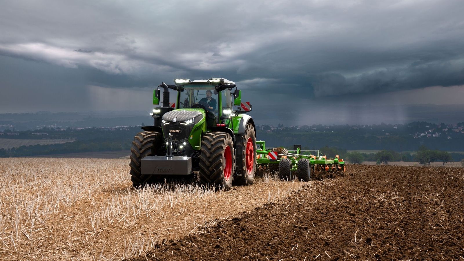 The Fendt 1000 Vario tractor is still doing field work at full power against heavy approaching storm clouds.