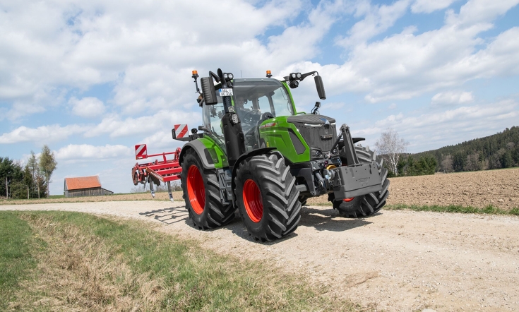 A Fendt 300 Vario with cultivator in transport A green Fendt 300 Vario driving with a red cultivator on a field path.