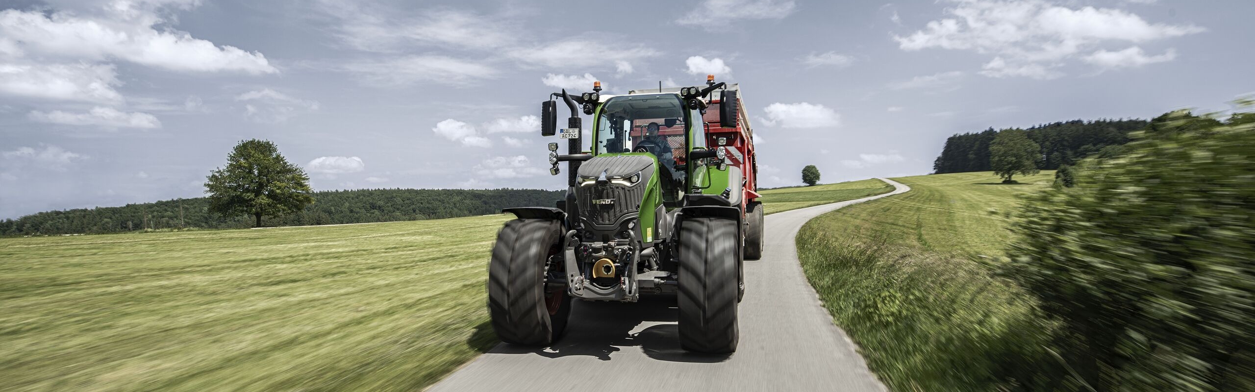 Een Fendt 700 Vario met opraapwagen rijdt in de zomer over een landweg