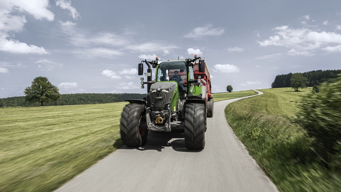 A Fendt 700 Vario Gen7.1 with attached forage wagon on a country road in the summer