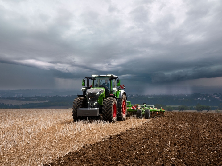The Fendt 1000 Vario tractor is still doing field work at full power against heavy approaching storm clouds.