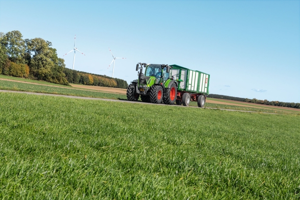 A green-painted Fendt tractor with a forage wagon driving over grassland