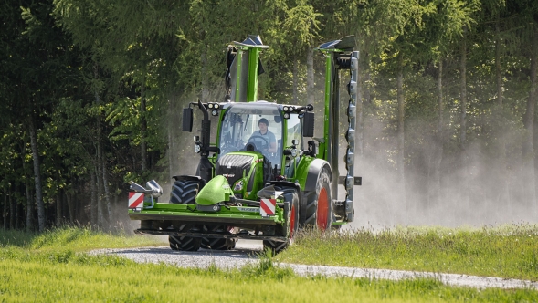 A green Fendt 500 Vario with implements driving from the field to a country road