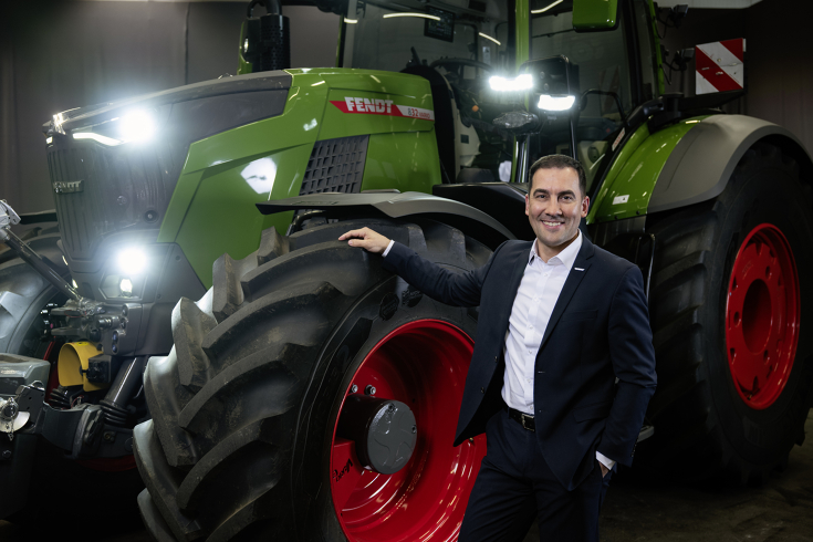 Dr Josef Mayer stands in a suit next to a large green tractor with red wheels.
