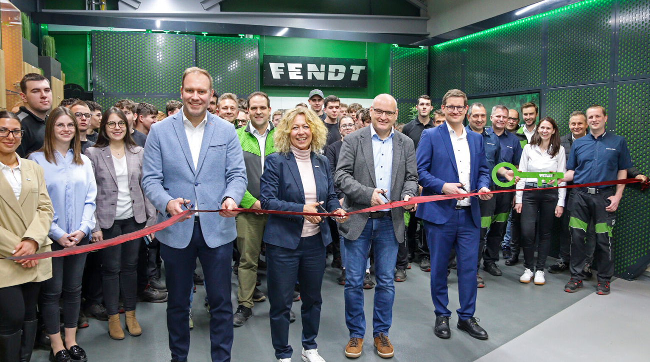A group of people, including four individuals in the foreground holding large scissors, cut a red ribbon in front of a Fendt sign in the new apprentice workshop.