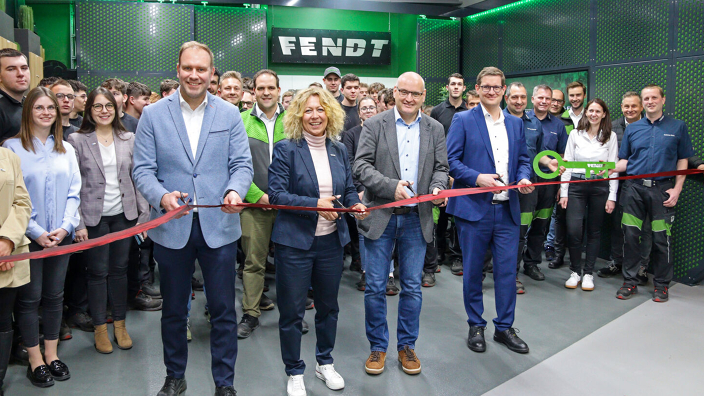 A group of people, including four individuals in the foreground holding large scissors, cut a red ribbon in front of a Fendt sign in the new apprentice workshop.