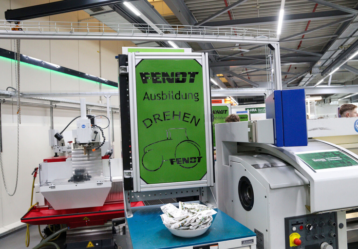 A green sign with the inscription "Fendt apprenticeship" hanging above machines in the Fendt training workshop.